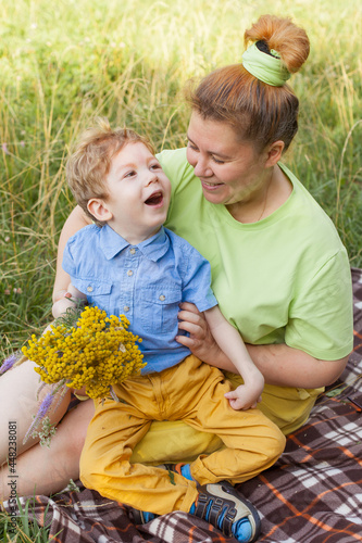 A small child in a wheelchair plays with his mother in the fresh air. Life in the educational age of disabled children,the concept of a happy disabled child.
