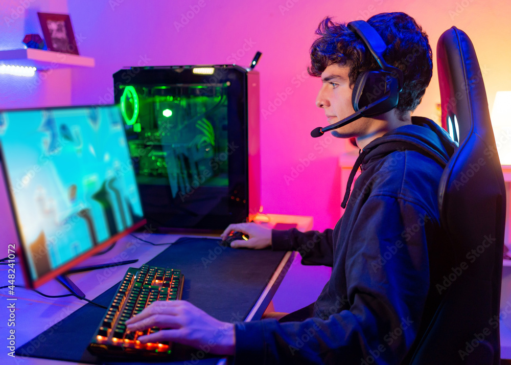 Fototapeta premium Caucasian young man in his room with colorful background plays video games on computer as hobby, entertainment and fun