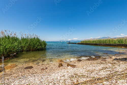 Beach and wooden pier with beach umbrella and empty deck chairs on Lake Garda, between the small villages of Lazise, Bardolino and Cisano. Tourist resort in Verona province, Veneto, Italy, Europe. photo