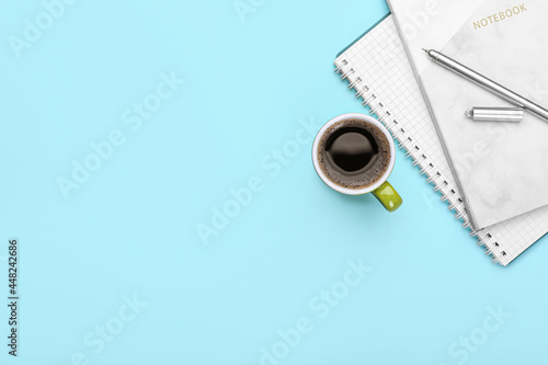 Cup of coffee, notebooks and pen on color background