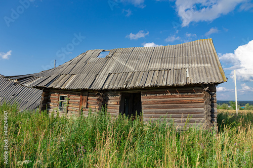 Old wooden rustic ruined abandoned house against a blue sky with white clouds on a bright summer sunny day. Close-up. Scenery