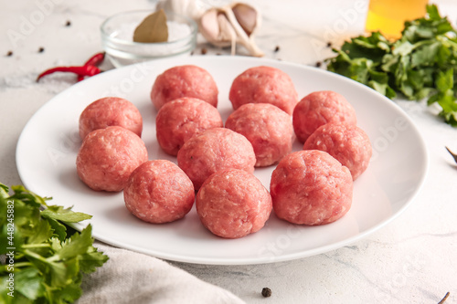 Plate with raw cutlets made of fresh forcemeat on light background