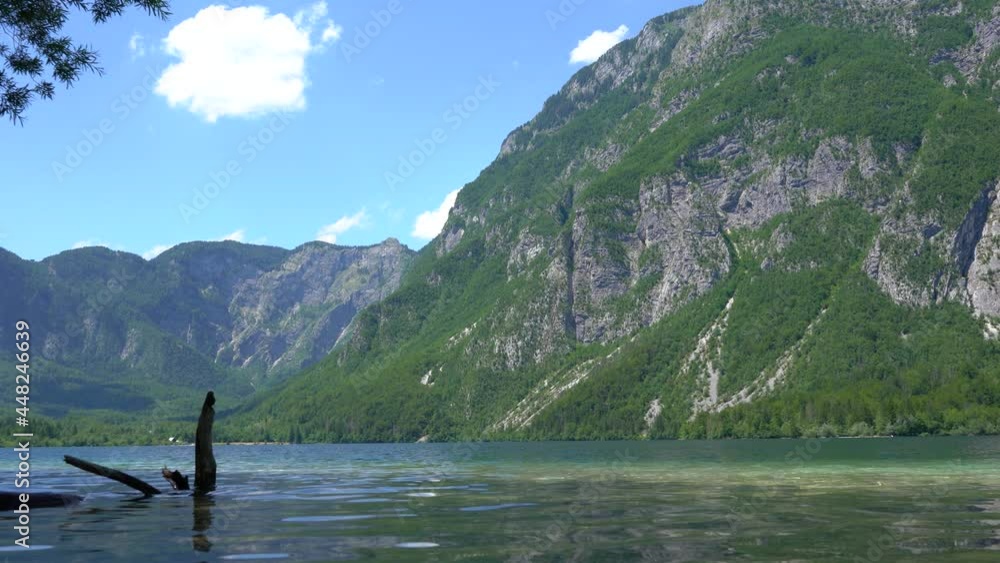Low angle view of calm Bohinj lake in Slovenia. Alpine lake surrounded with steep Alps. Dense forest covering the mountains. Calm waves in glacial lake. Static shot, real time, wide angle Low angle view of calm Bohinj lake in Slovenia. Alpine lake surrounded with steep Alps. Dense forest covering the mountains. Calm waves in glacial lake. Static shot, real time, wide angle