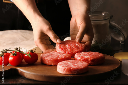 Woman preparing tasty cutlets made of fresh forcemeat on dark background