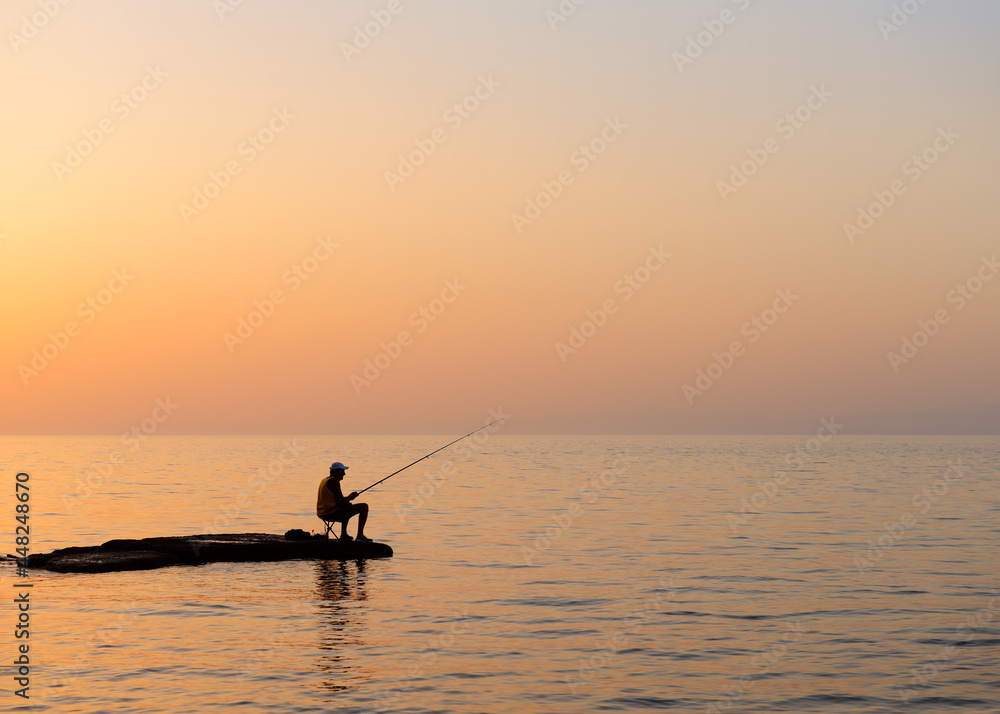 Naklejka premium Fisherman silhouetted against a dusk sky