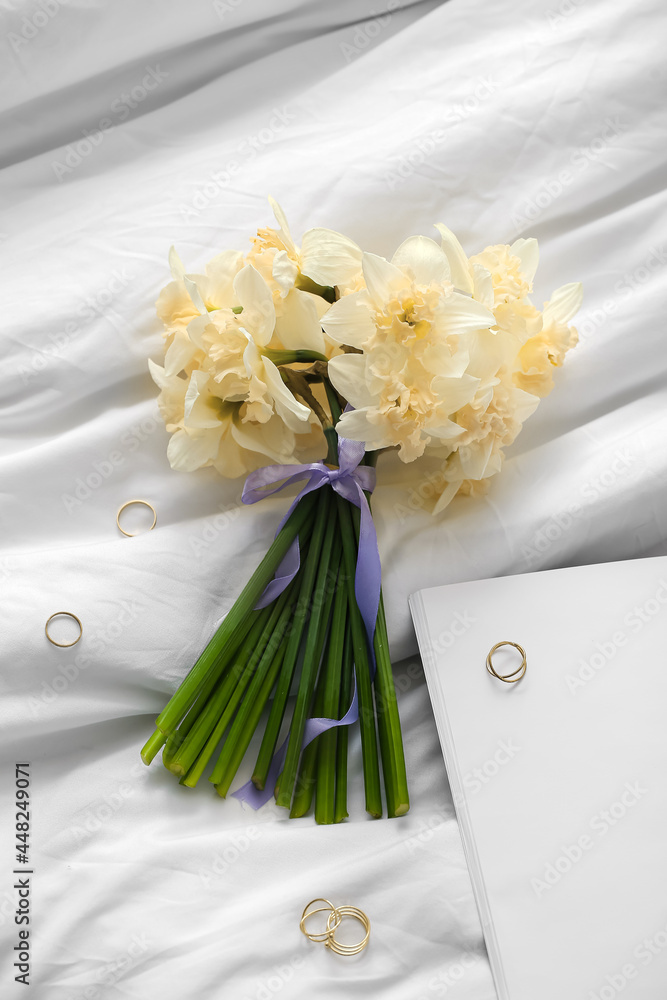 Beautiful bouquet of narcissus flowers with golden rings on bed Stock