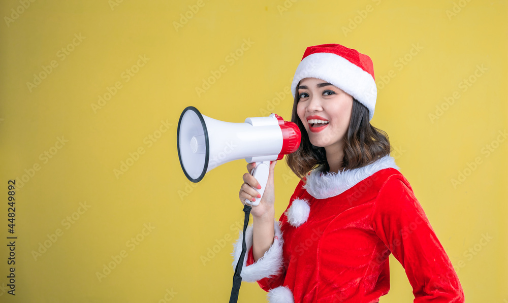 Portrait of beautiful young Asian woman in santa claus clothes and hat with megaphone isolated on yellow background. Portrait of beautiful young Asian woman in santa claus clothes and hat with megaphone isolated on yellow background.