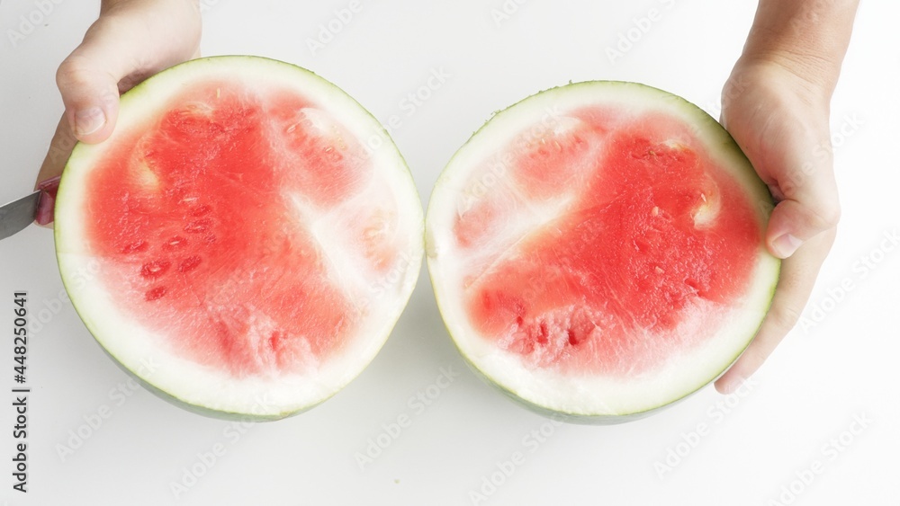A beautiful green watermelon on a white background. A man cuts a watermelon into two parts with a knife and opens it, the red pulp of a watermelon with white veins of netrat appears in the frame. 