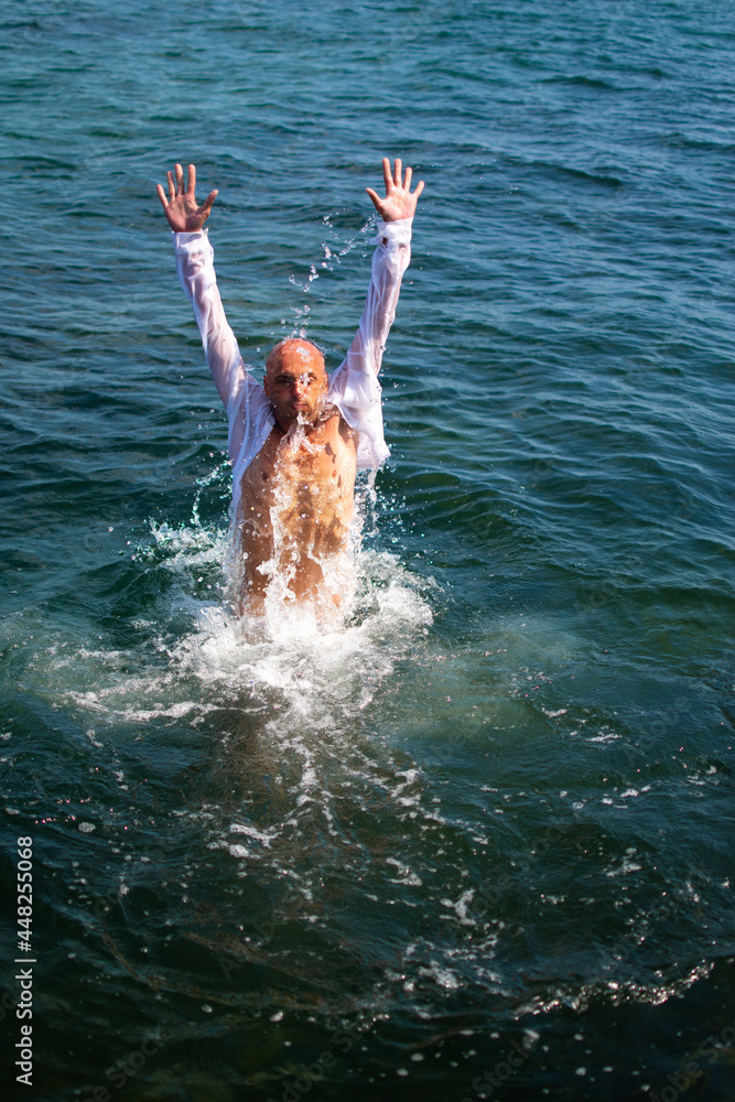 Adult man diving in the sea in wet white shirt