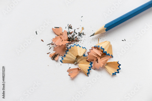 Blue pencil and its shavings, crumbs and dusts on white paper.