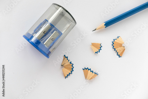 Blue pencil with pencil sharpener and its shavings on white paper background.