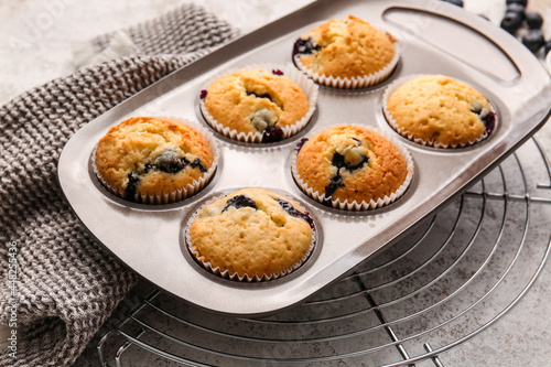Baking tin with tasty blueberry muffins on light background