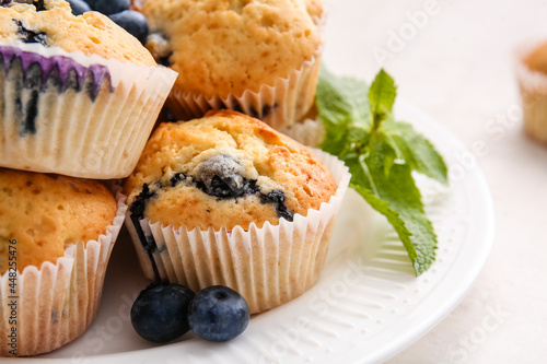 Plate with tasty blueberry muffins on light background, closeup
