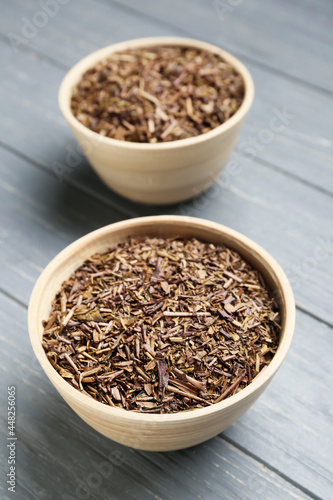Bowls of dry hojicha green tea on grey wooden background