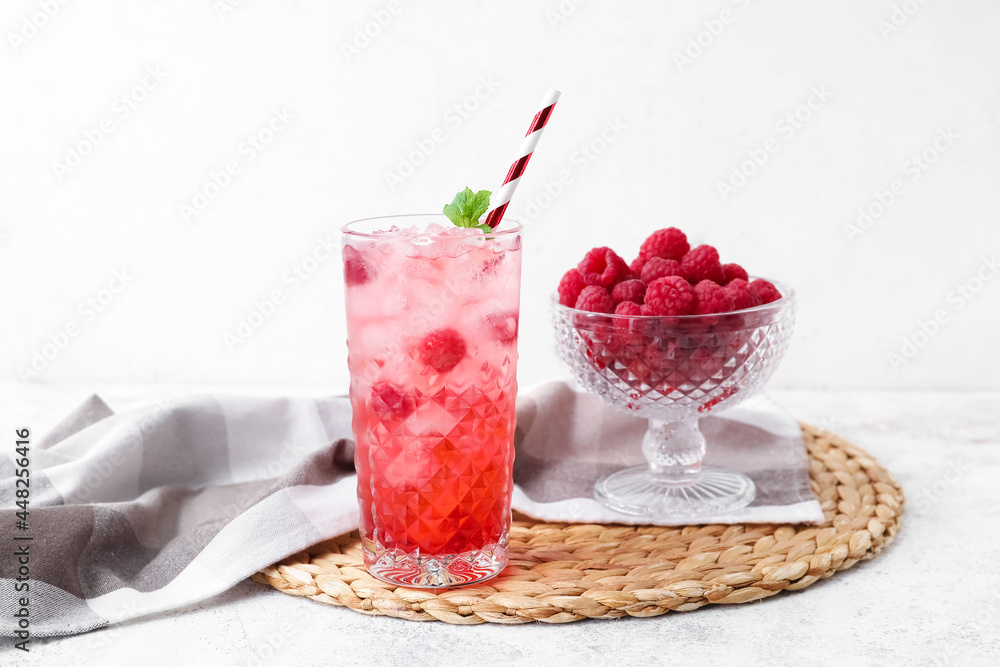 Glass of tasty lemonade and bowl with raspberry on light background Glass of tasty lemonade and bowl with raspberry on light background