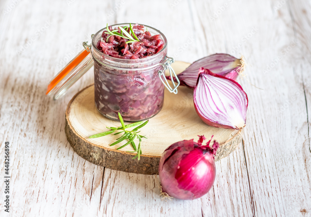 Red onion marmalade placed on wooden trunk with wood texture background. Jam from onion is delicious part of French cuisine. Homemade jam in transparent glass, vibrant colors, soft light.