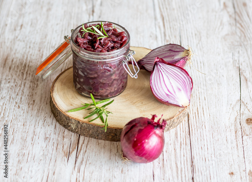 Fototapeta Naklejka Na Ścianę i Meble -  Red onion marmalade placed on wooden trunk with wood texture background. Jam from onion is delicious part of French cuisine. Homemade jam in transparent glass, vibrant colors, soft light.