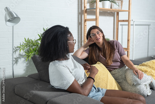 Two young women mixed race college students roommates sitting at their rented apartment and having a conversation on the weekend sharing their positive energy photo