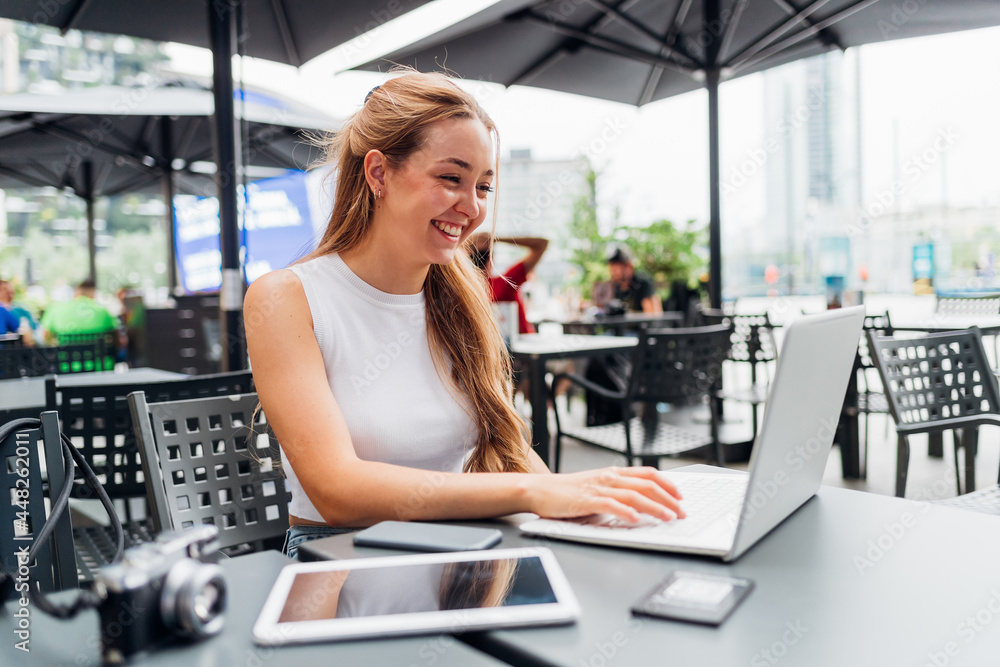 young caucasian woman sitting outdoors using computer and technological devices smiling working or shopping