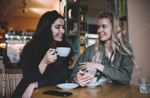 Delighted multiethnic friends with smartphone and cups of coffee