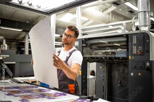 Print shop worker checking quality of imprint and controlling printing process.