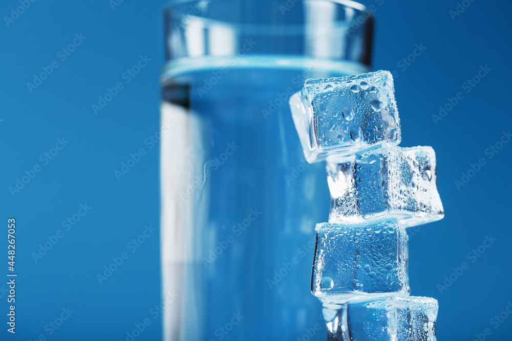 Ice cubes tower with a glass of cold and clean water on a blue background. Ice cubes tower with a glass of cold and clean water on a blue background.