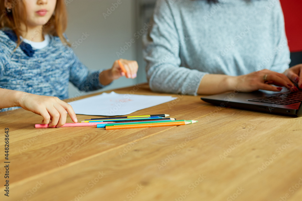 Mother working in her home office on a laptop, her daughter sits next to her and draw Mother working in her home office on a laptop, her daughter sits next to her and draw