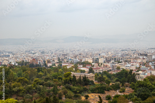 View on Temple of Hephaestus in greenery and Athens ancient city center with white buildings on gray foggy day from Areopagus Hill near Acropolis