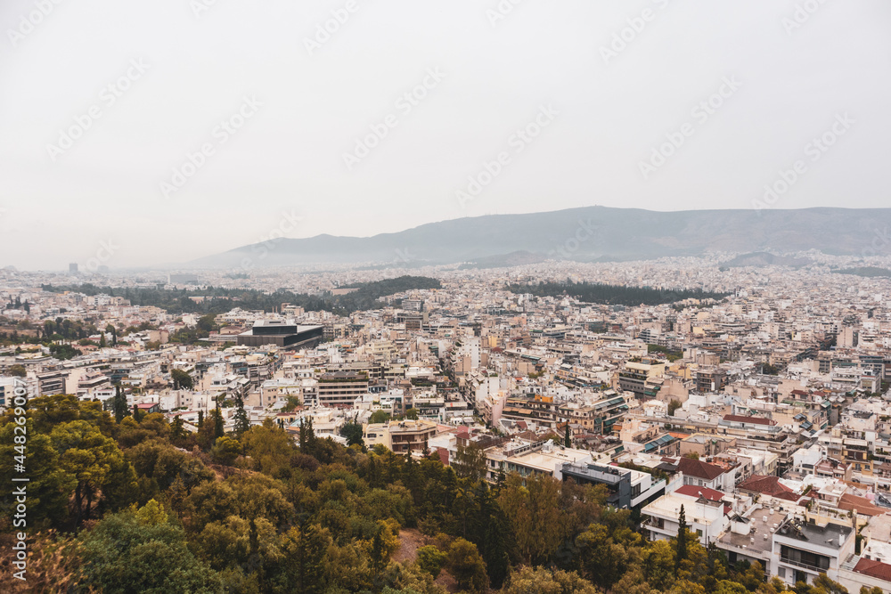 Athens city center streets with white buildings in parks greenery on gray foggy day. Rooftop view from Filopappou Hill park near Acropolis, Greece
