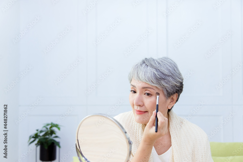 Senior Asian woman is looking at the mirror and paint her eyebrows. Senior Asian woman is looking at the mirror and paint her eyebrows.