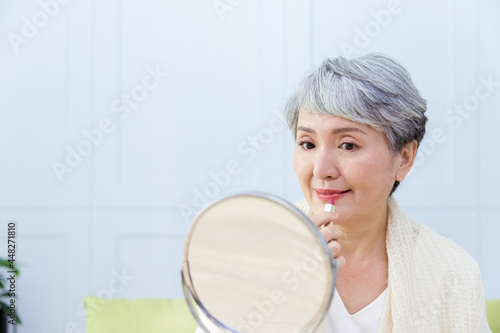 Senior Asia woman is looking at the mirrior and applying lipstick. photo