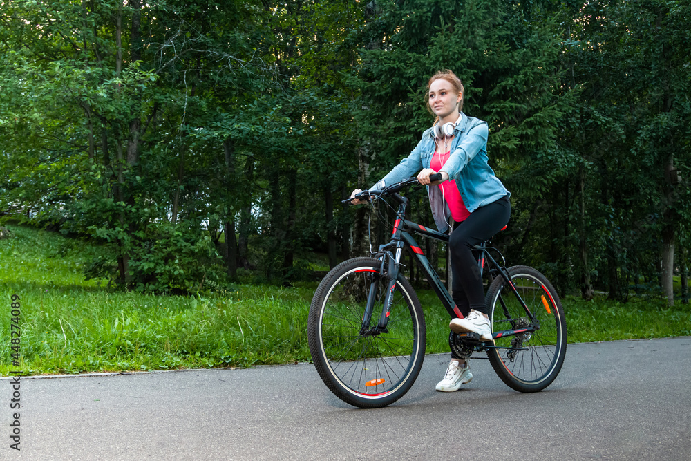 The girl rides a bike in the park. Beautiful redhead girl in the park.