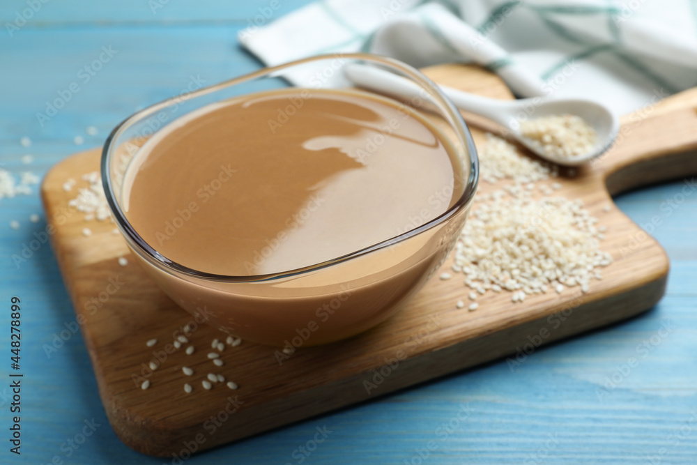 Tasty sesame paste and seeds on light blue wooden table Tasty sesame paste and seeds on light blue wooden table