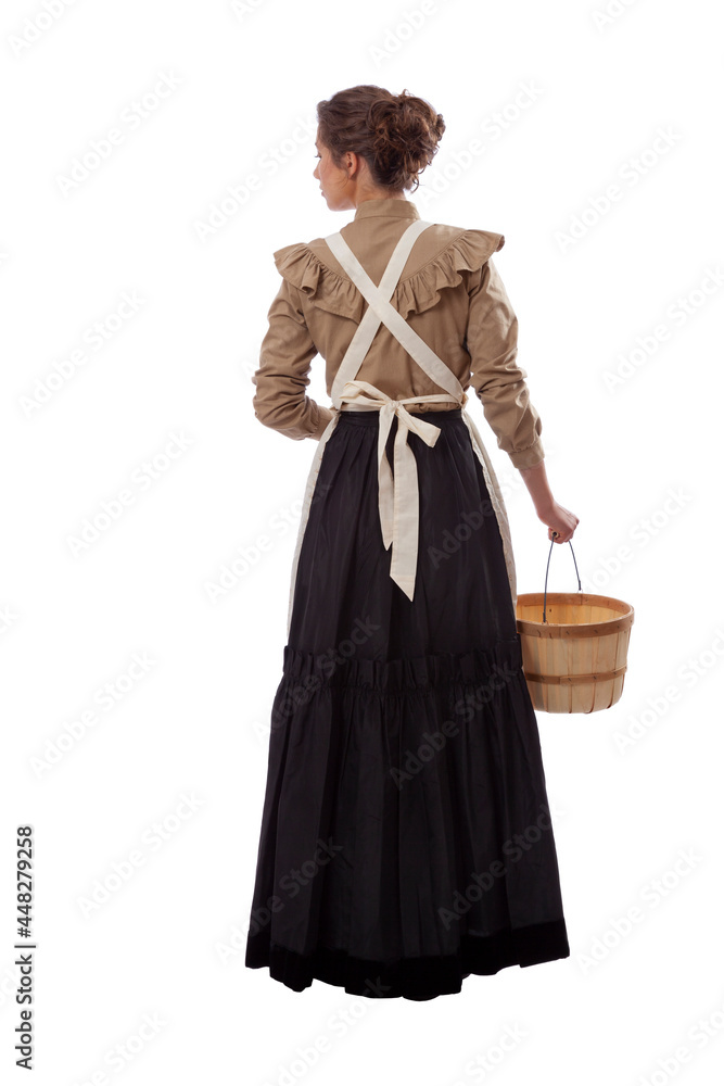 Young prairie woman in apron facing away looking left holding a basket isolated on white