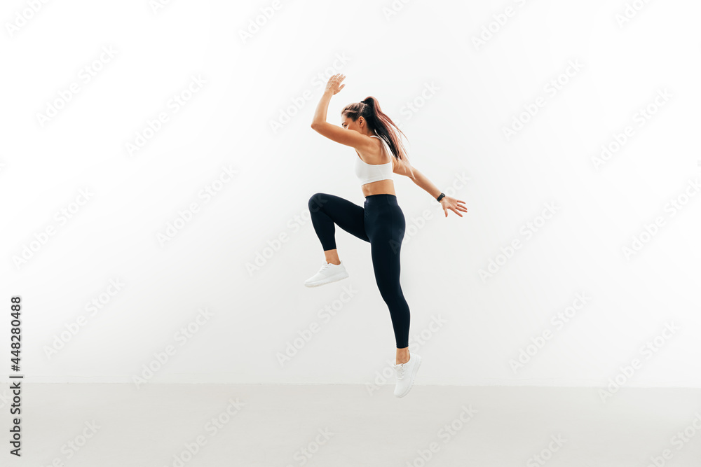 Sportswoman jumping up indoors. Female athlete warming up against a white wall.