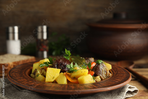 Tasty cooked dish with potatoes in earthenware on wooden table
