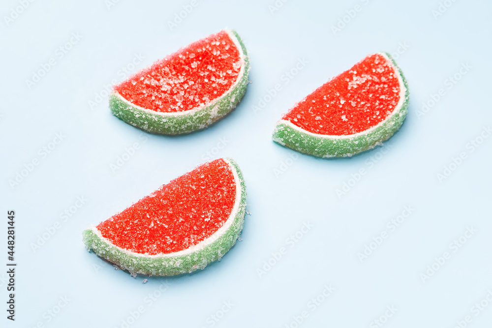 Jelly candies. Three watermelon jelly candies sprinkled with sugar on a blue background. Watermelon marmalade. Selective soft focus. Jelly candies. Three watermelon jelly candies sprinkled with sugar on a blue background. Watermelon marmalade. Selective soft focus.