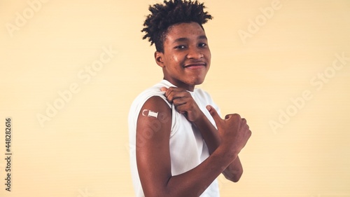 African American teenager showing COVID-19 vaccine bandage merrily in concept of coronavirus vaccination program to vaccinate citizen .