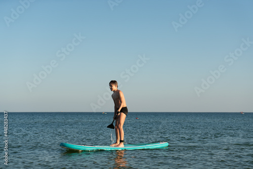 A 12 year old boy learns to stand on a SUP board in the sea near the shore.