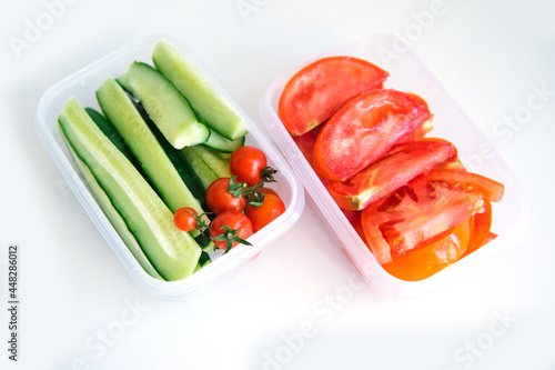 Sliced vegetables in plastic containers on a white background. Cucumbers and tomatoes are in containers.