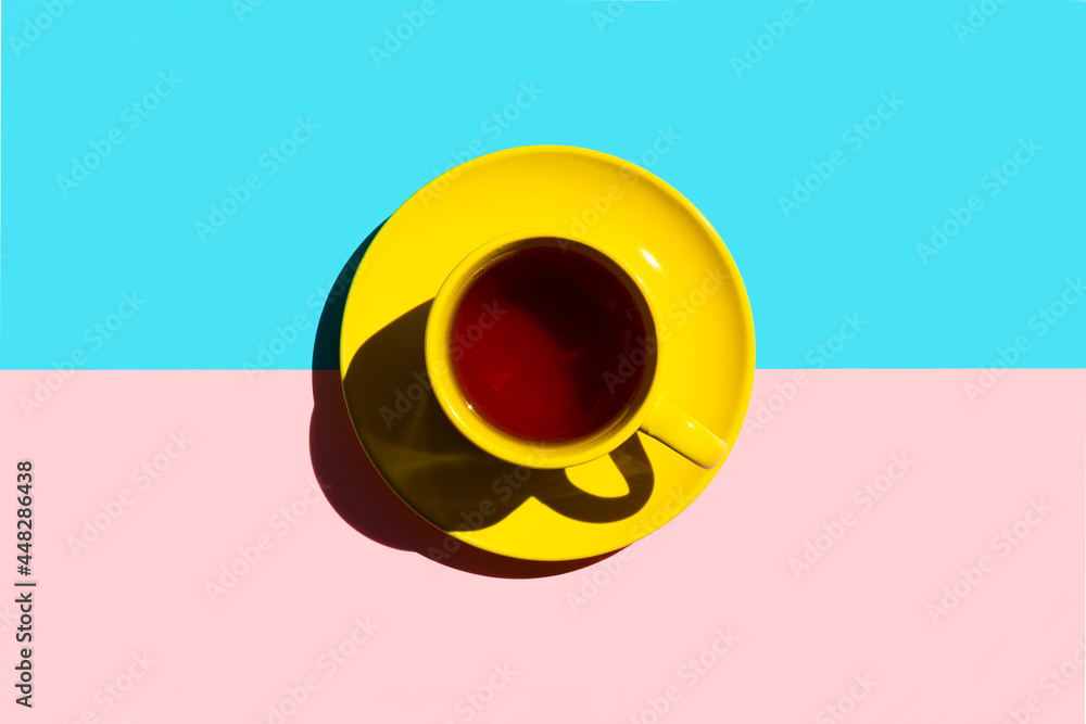 yellow cup saucer with black tea or coffee on the colour background with pink and blue. copy space. top view