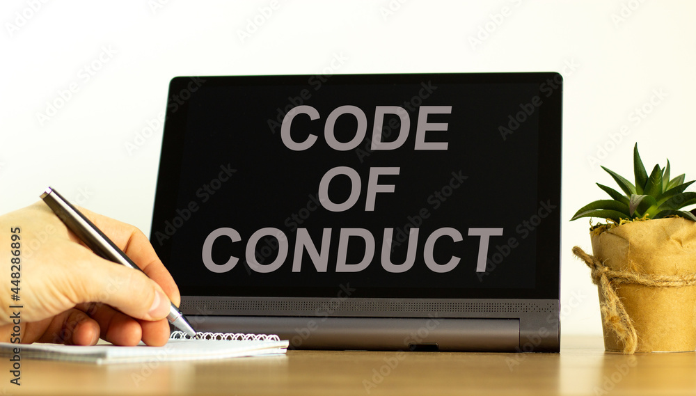 Code of conduct symbol. Tablet with words 'code of conduct'. Businessman hand with pen, house plant. Beautiful white background. Business, code of conduct concept, copy space. Code of conduct symbol. Tablet with words 'code of conduct'. Businessman hand with pen, house plant. Beautiful white background. Business, code of conduct concept, copy space.