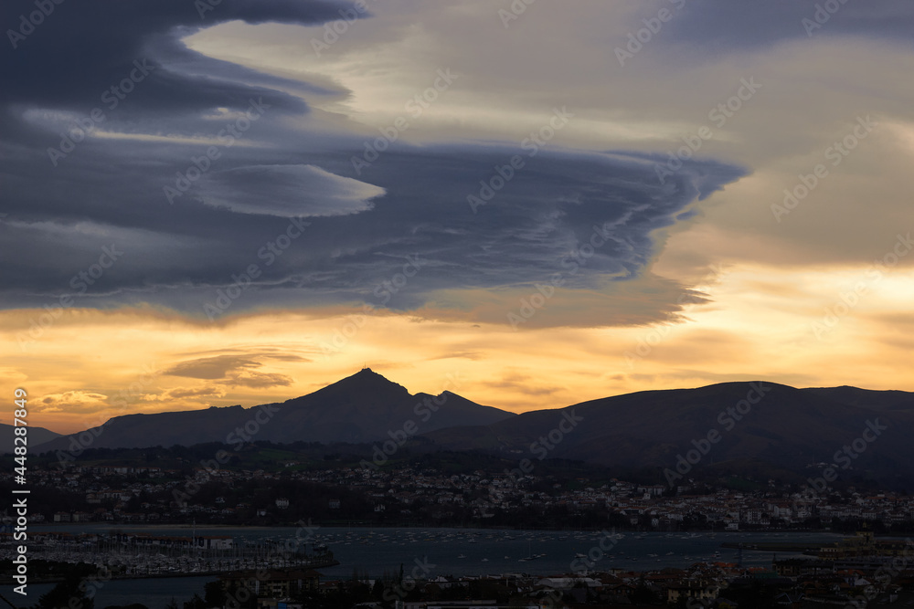 panoramic of a town with its nearby mountains and a sky with clouds colored by sunrise