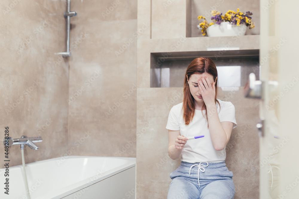 young frustrated woman looking at a quick positive or negative result pregnancy test sitting in bathroom by a unwanted. Female expectant mother sitting at home sad and disappointed young frustrated woman looking at a quick positive or negative result pregnancy test sitting in bathroom by a unwanted. Female expectant mother sitting at home sad and disappointed