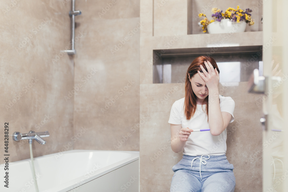 young frustrated woman looking at a quick positive or negative result pregnancy test sitting in bathroom by a unwanted. Female expectant mother sitting at home sad and disappointed young frustrated woman looking at a quick positive or negative result pregnancy test sitting in bathroom by a unwanted. Female expectant mother sitting at home sad and disappointed
