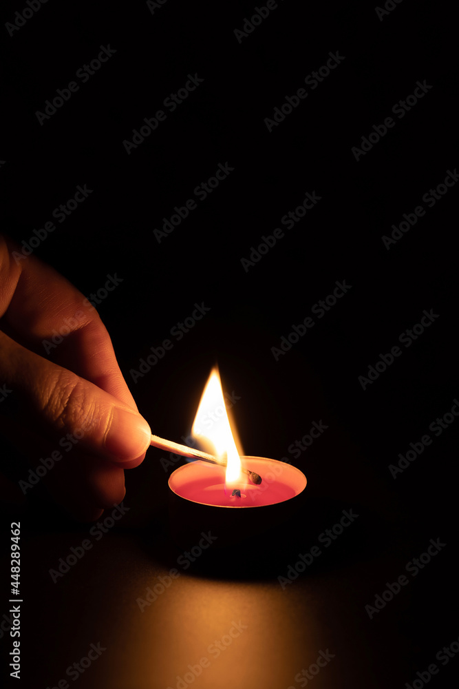 Lighting a red candle with a match in the dark. Memory concept. Black background, vertical orientation.