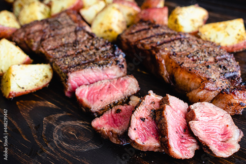 Grilled NY Strip Steak with Coffee Rub and Roasted Potatoes: Grilled New York strip steaks with roasted potatoes on a dark wood background