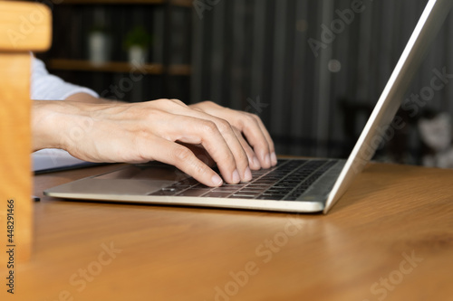 Side view and close up of young woman hands are typing on the modern laptop computer keyboard on wooden office table desktop with supplies for business and technology concept.