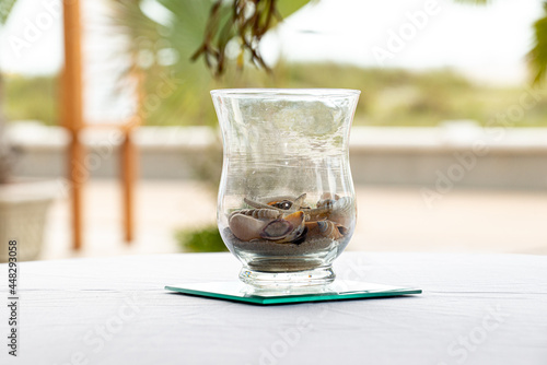 Glass vase centerpiece filled with seashells on white table outdoors near beach