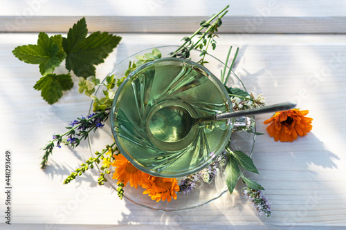 Herbal tea in a cup and flowers and leaves of mint, calendula, thyme, currant, clover on a light wooden background, top view.